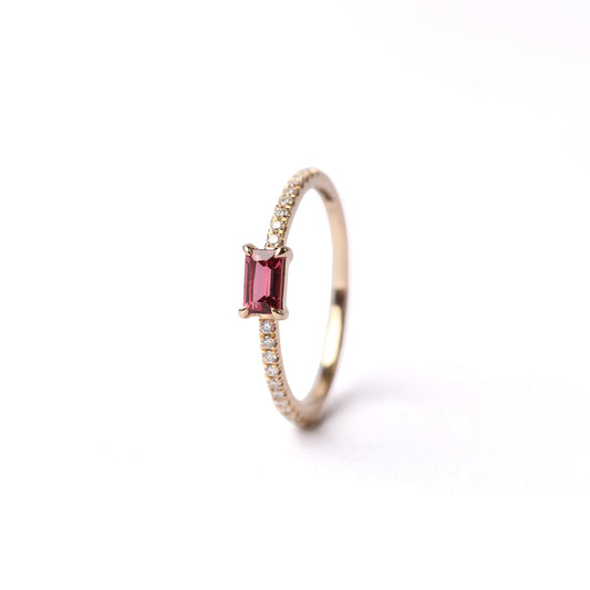 Women's solid yellow gold ring set with a baguette cut pink tourmaline gemstone, with small round diamonds on either side of the shoulders of the ring, displayed standing up, front facing on a white background.