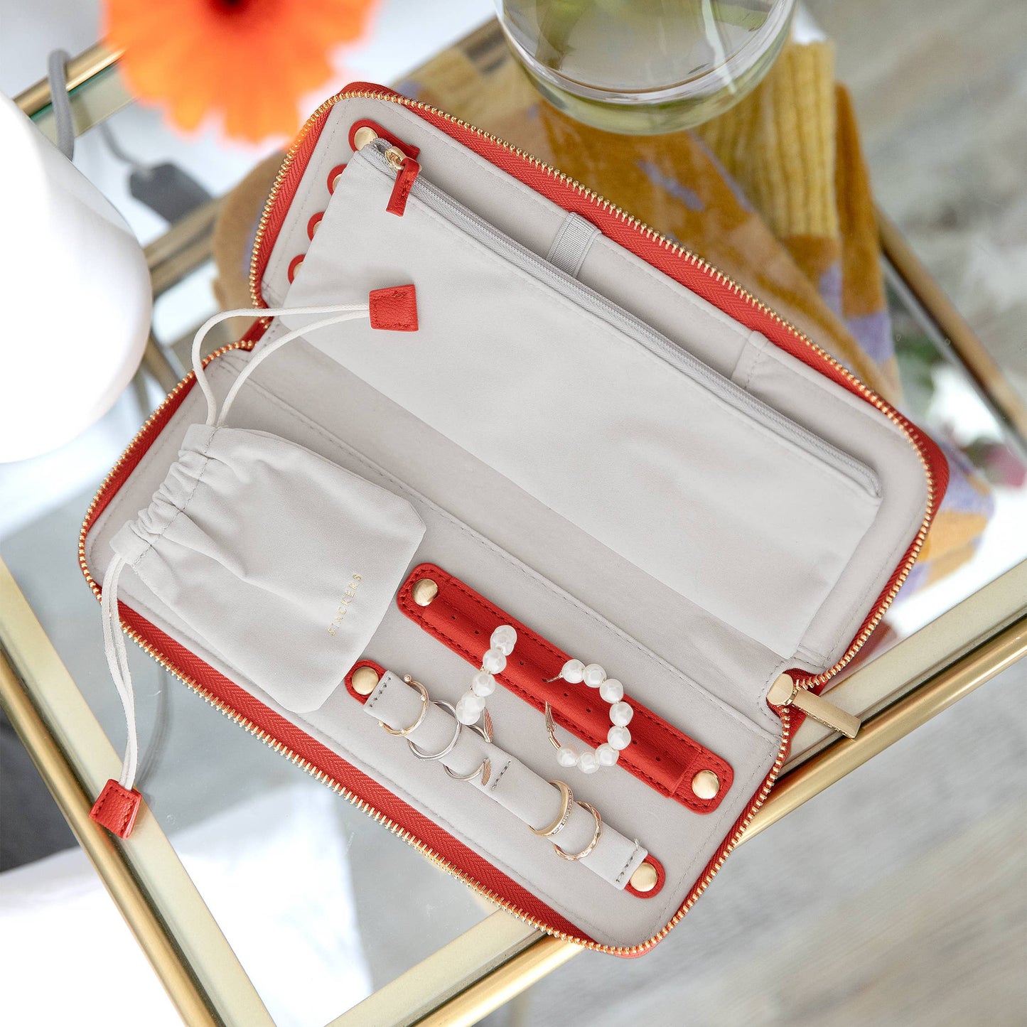 Open red and white jewelry box on a reflective surface with flowers in the background