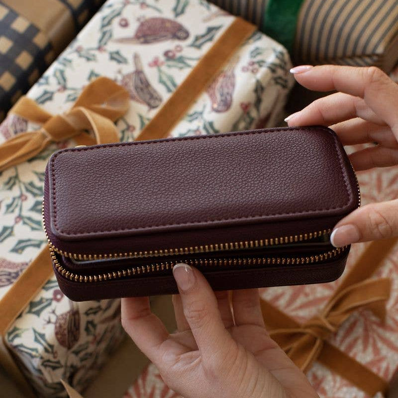 Medium burgundy Stackers travel jewellery case held by hands with gifts in the background