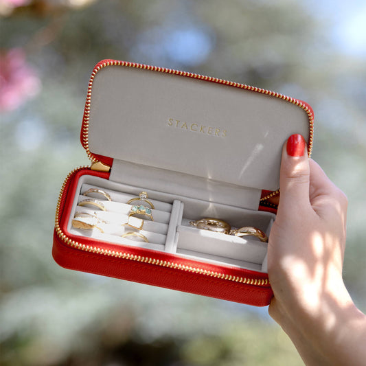 Medium red travel jewellery case with gold rings held by a hand against a blurred natural background