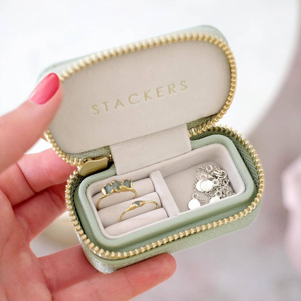 Mini mint green Stackers travel jewellery box containing rings and a necklace, held by a hand.