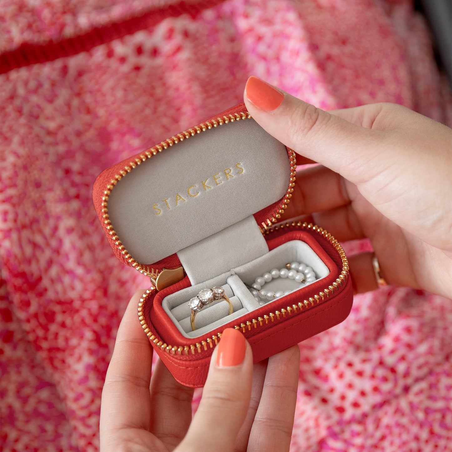 Red jewelry case with gold zipper held by a person, displaying Stackers brand.