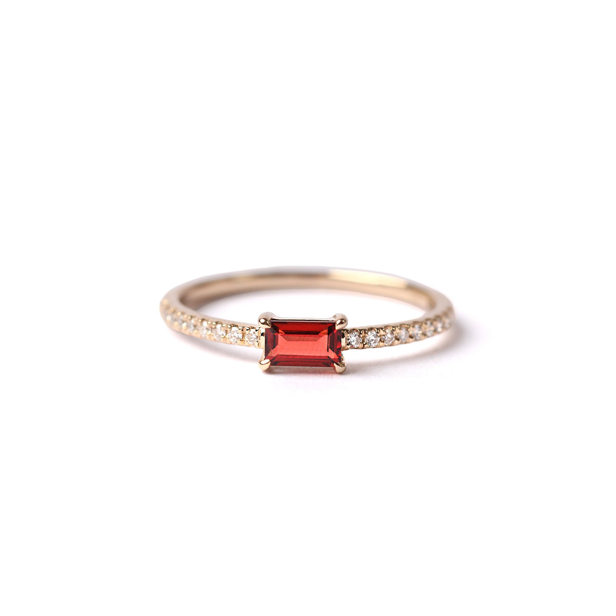 Women's solid yellow gold ring set with a central baguette cut red garnet, with small round diamonds each side set into the shoulders of the band, displayed laying down, facing frontwards on a white background.