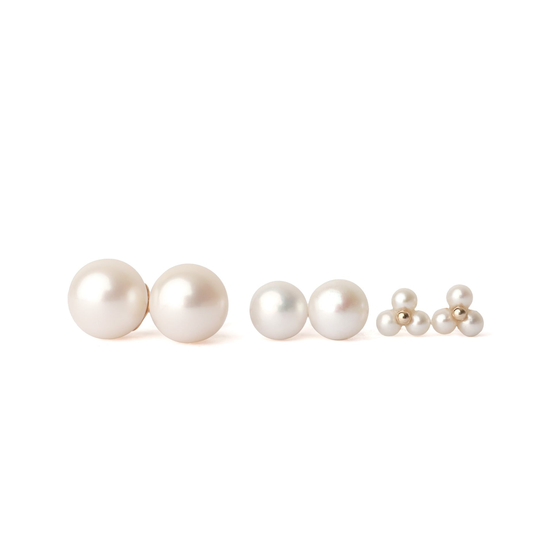 Three pairs of solid yellow gold and freshwater pearl earrings . The first set is classic size, the middle set is small, the third set is three tiny pearls surrounding a gold centre. The pairs are facing forward and set on a white background for the shopper to view.