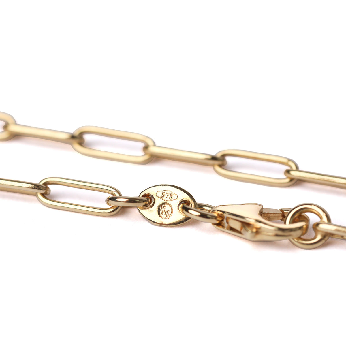 A close-up of a gold paperclip chain necklace with a lobster clasp and a circular hallmark tag, shown on a plain white background.