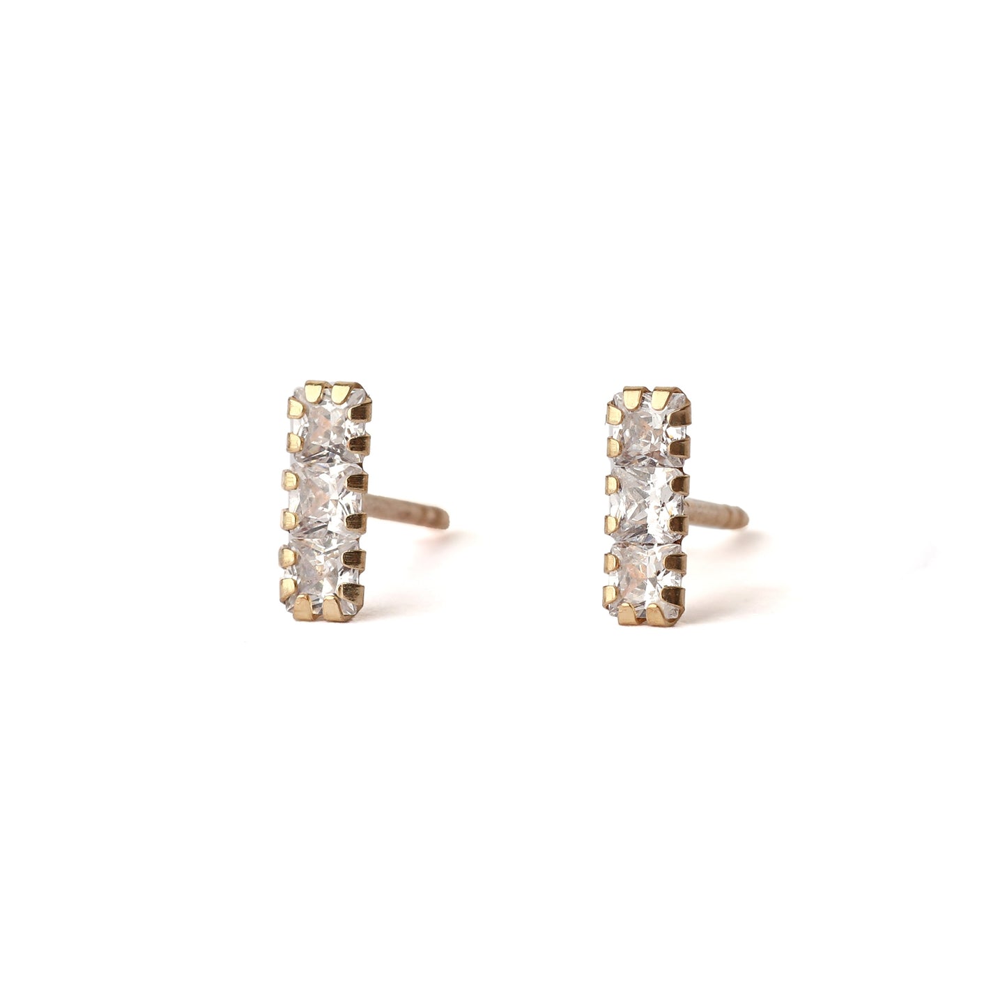 A pair of solid yellow gold studs with three small cubic zirconia gemstones in each, set in a rectangle shape. The earrings dace forward and are displayed for the shopper on a white background.
