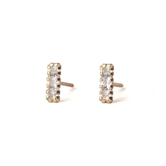 A pair of solid yellow gold studs with three small cubic zirconia gemstones in each, set in a rectangle shape. The earrings dace forward and are displayed for the shopper on a white background.