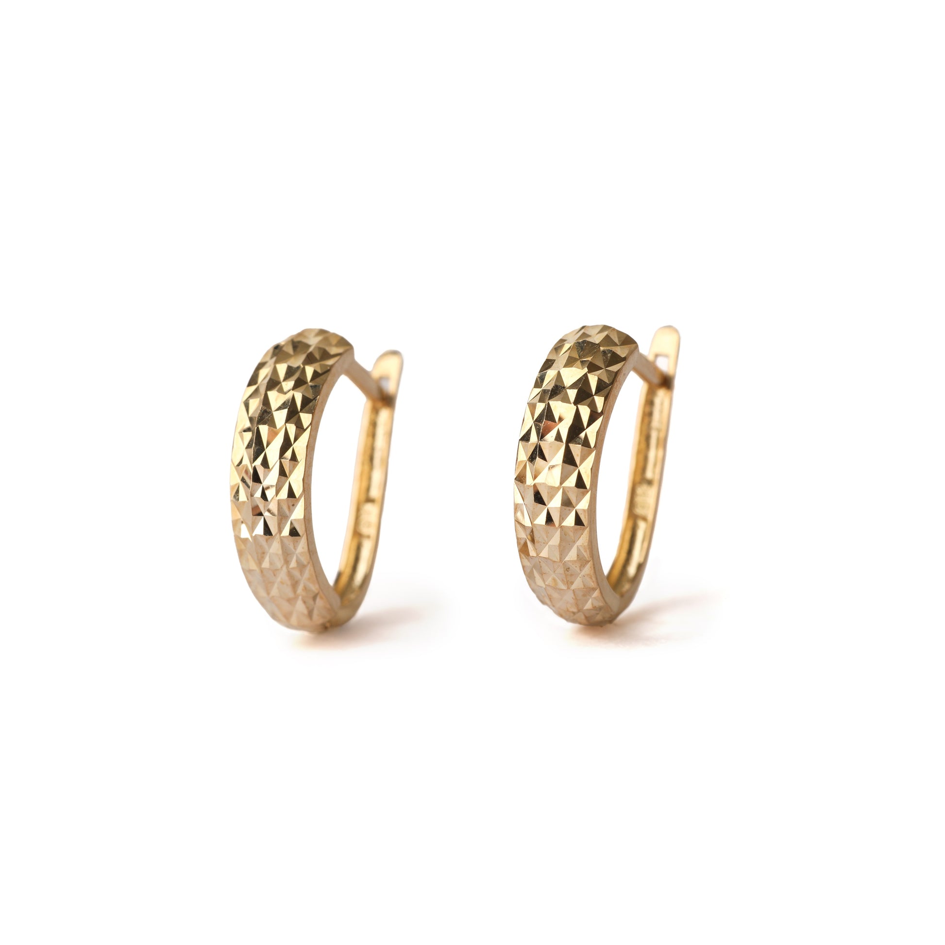 A pair of solid yellow gold huggie hoop earrings with a diamond cut design on the front. Both face straight on and are set on white background for the shopper to view.