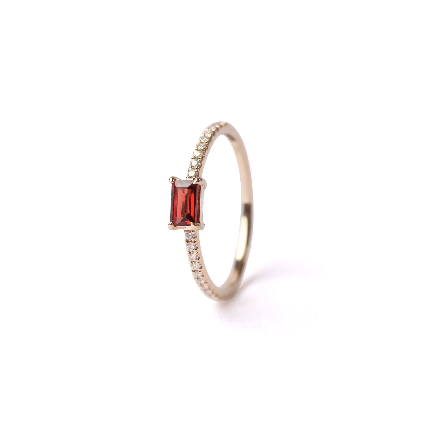 Women's solid yellow gold ring set with diamonds on the shoulders and a central red baguette cut garnet gemstone, displayed on it's side, front facing, on a white background.