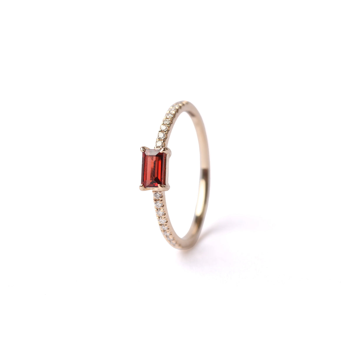 Women's solid yellow gold ring set with diamonds on the shoulders and a central red baguette cut garnet gemstone, displayed on it's side, front facing, on a white background.
