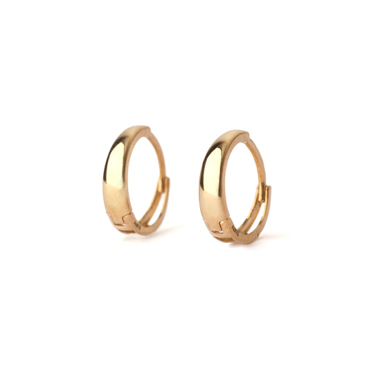 A pair of solid yellow gold huggie hoop earrings on a white background both facing forward.
