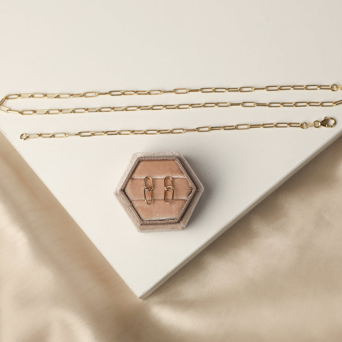 Women's solid yellow gold paperclip style chain bracelet, earrings and necklace displayed on a beige background.