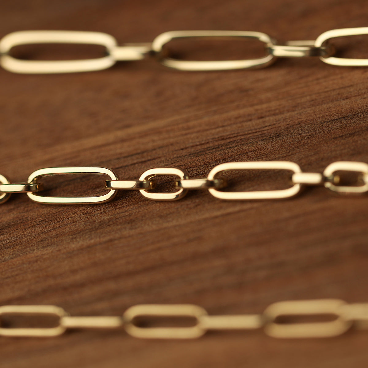 Three women's solid yellow gold chain bracelets displayed in rows on a wooden background.